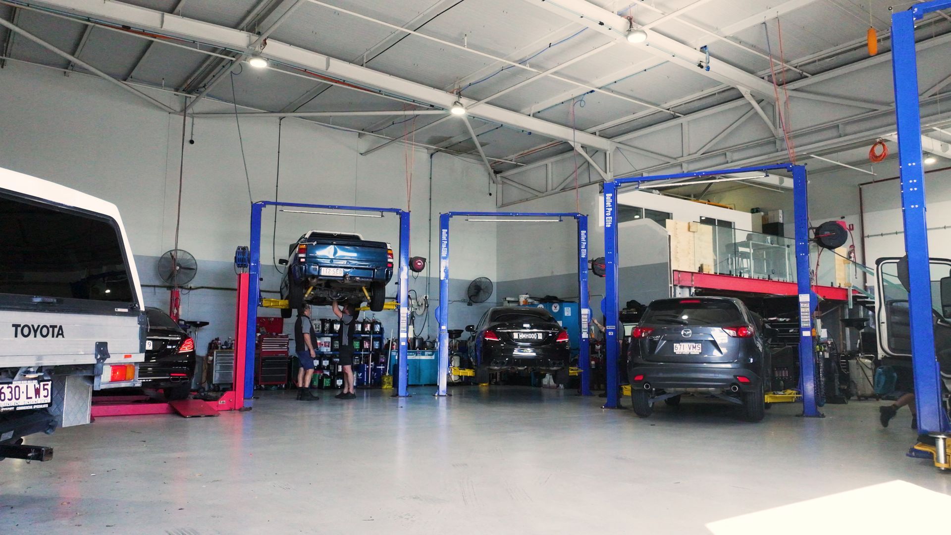 Indoor auto repair shop with several cars on lifts and a white van in a spacious garage