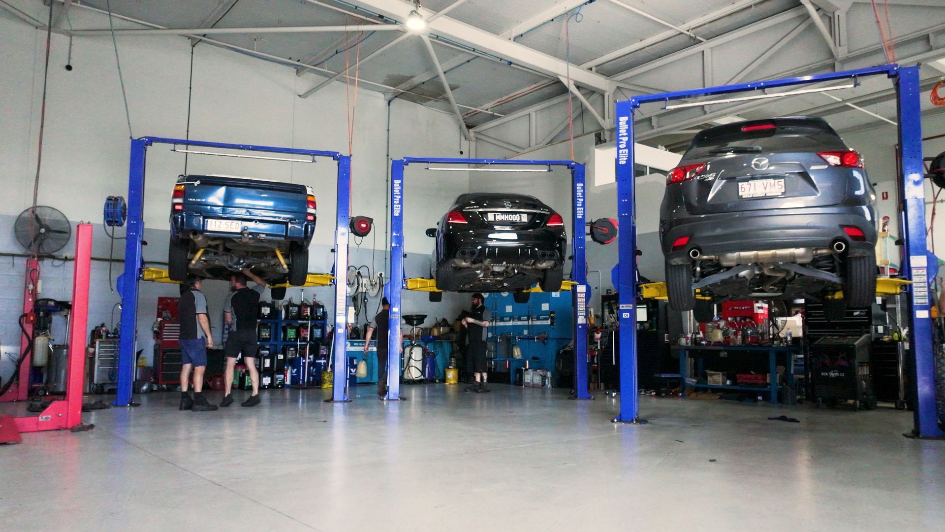 Three cars on lifts in an auto repair shop, with mechanics working beneath them.