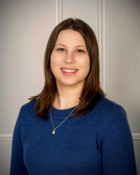 Portrait of a smiling woman in a blue sweater against a neutral gray background