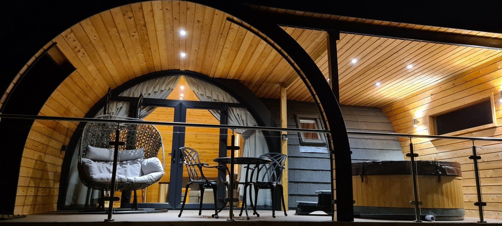 A wooden hut with a table and chairs on a balcony at night.