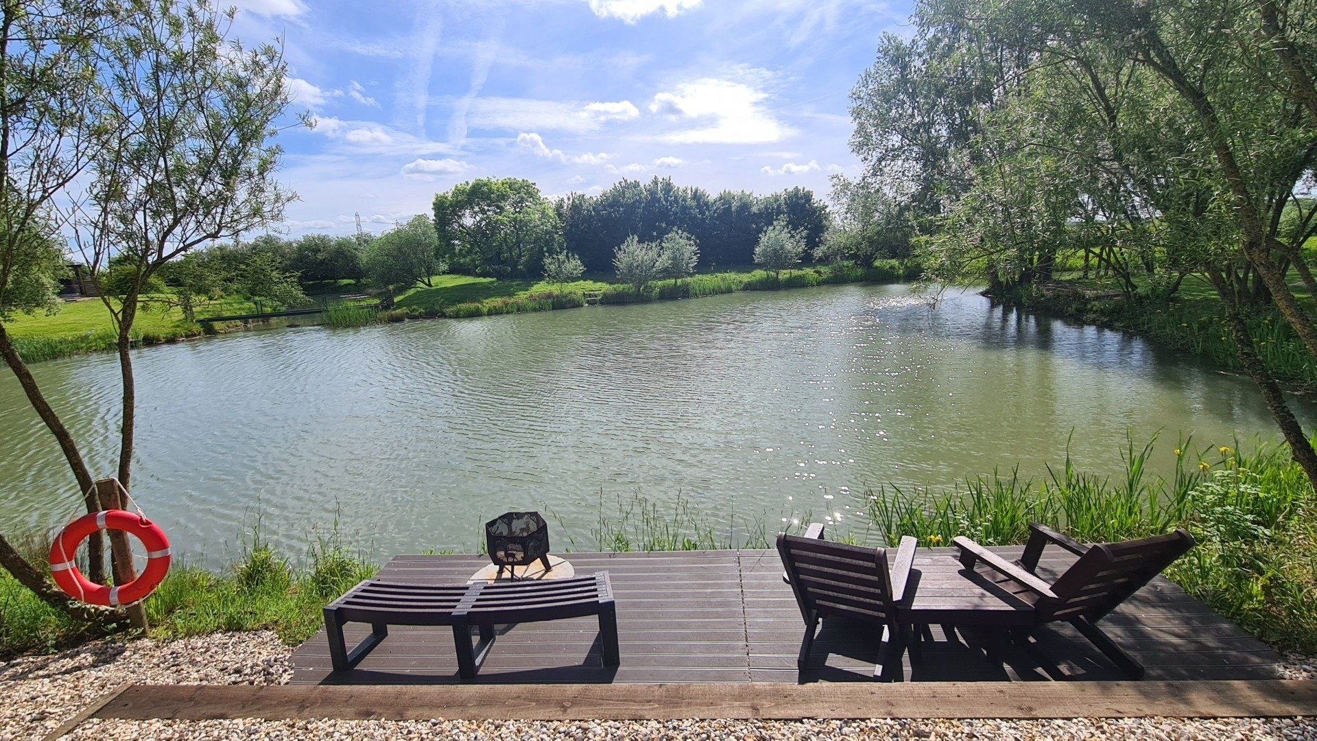 A wooden deck with chairs and a table overlooking a lake.