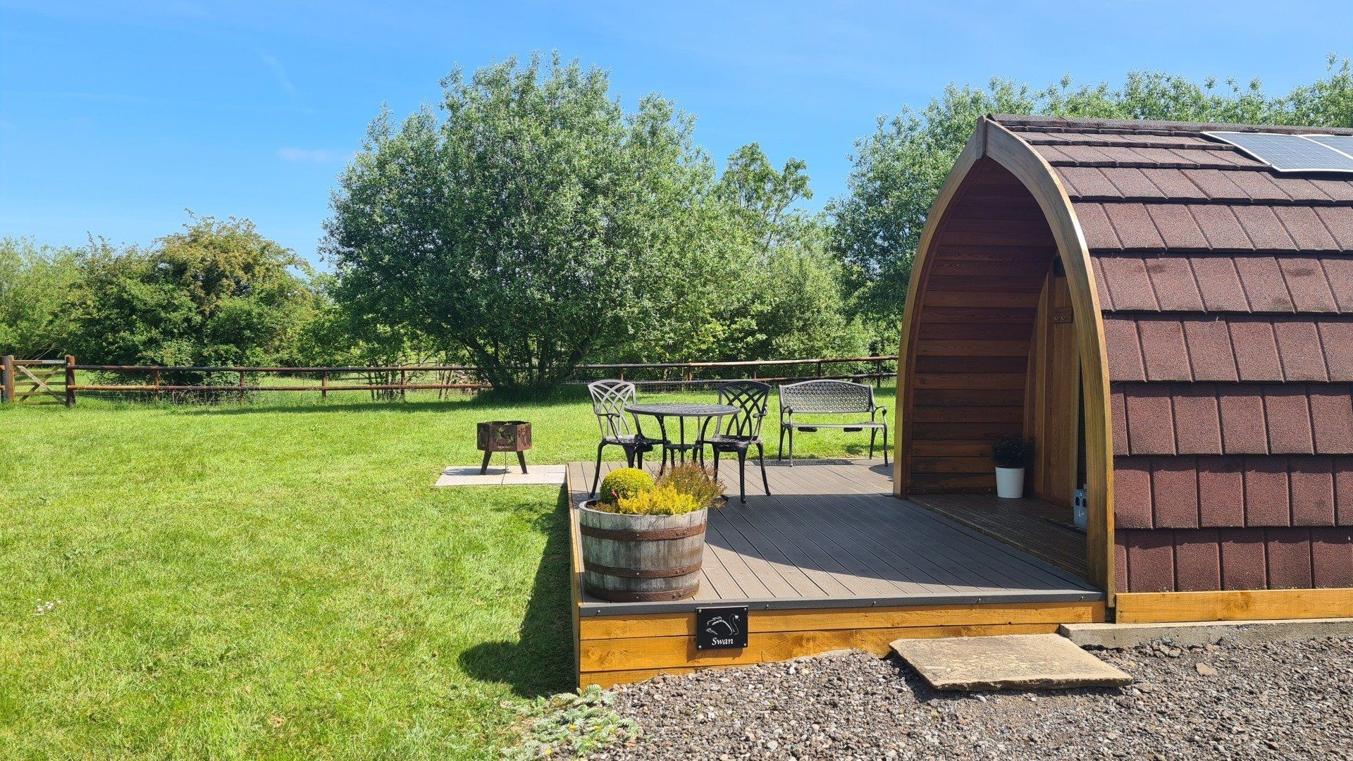 A small wooden shack with a deck in the middle of a grassy field.