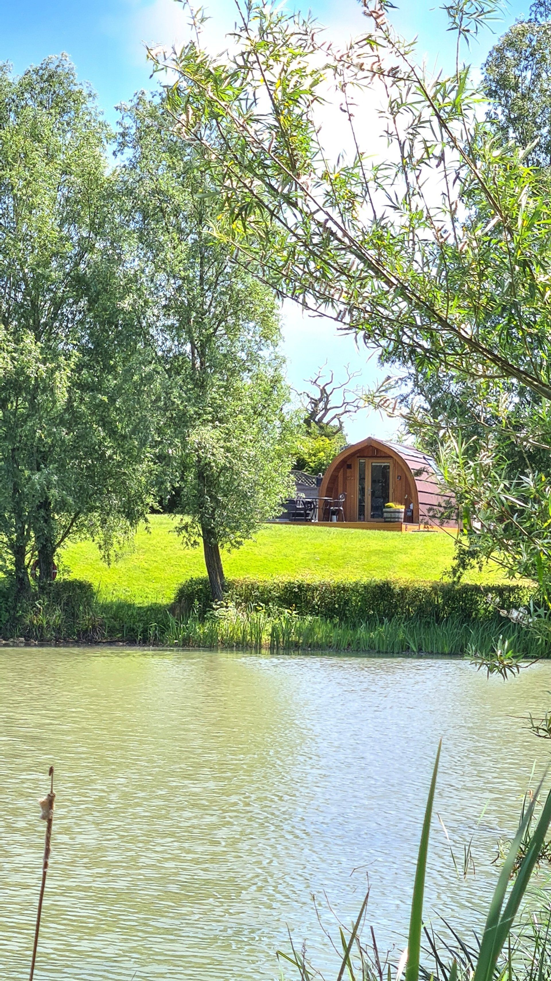 A tent is sitting on top of a grassy hill next to a lake.