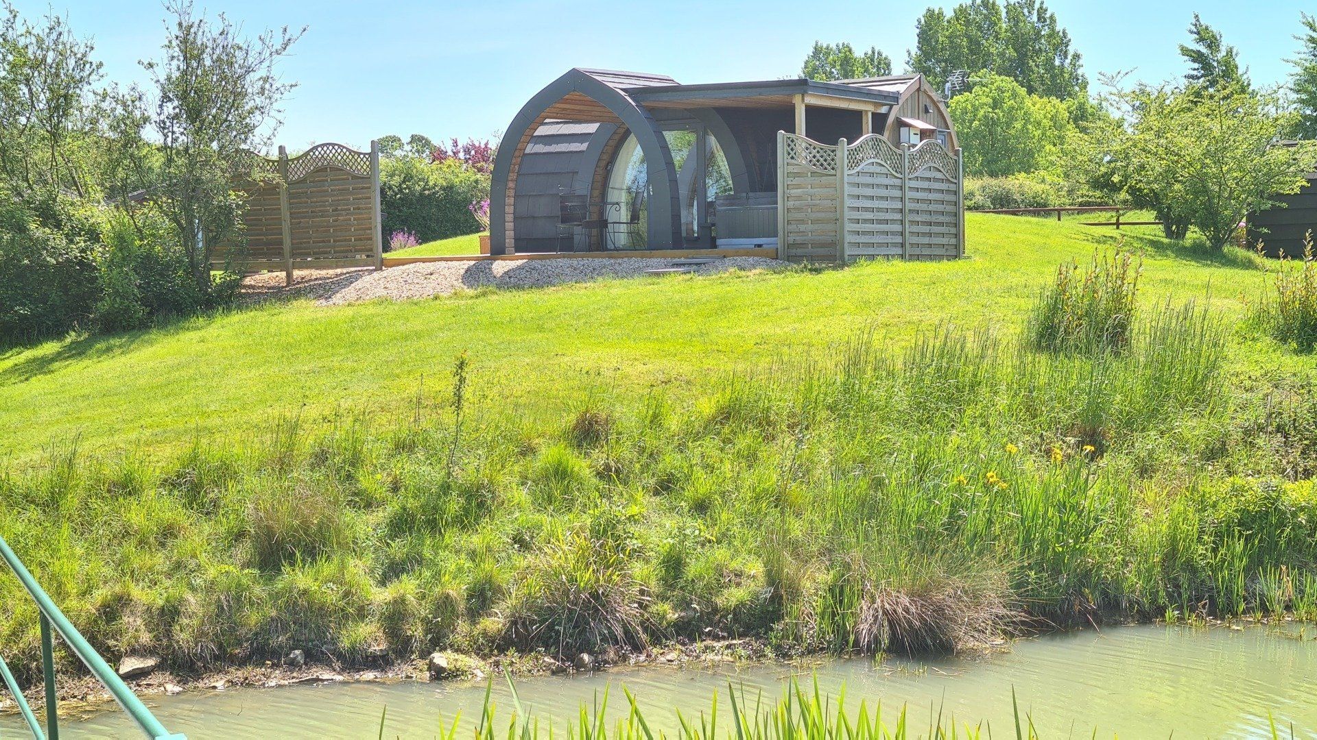 A small house is sitting on top of a grassy hill next to a body of water.