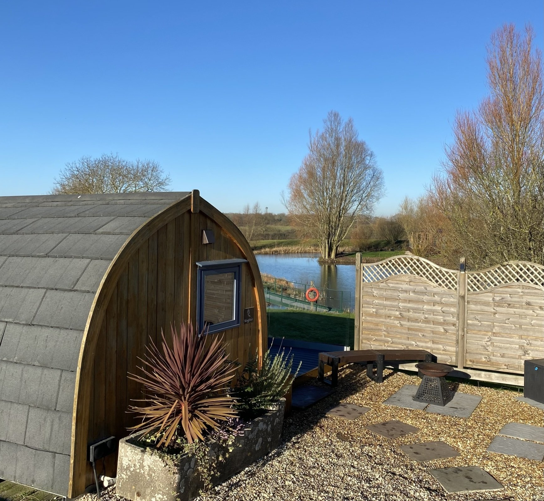 A wooden shed with a slate roof sits next to a lake