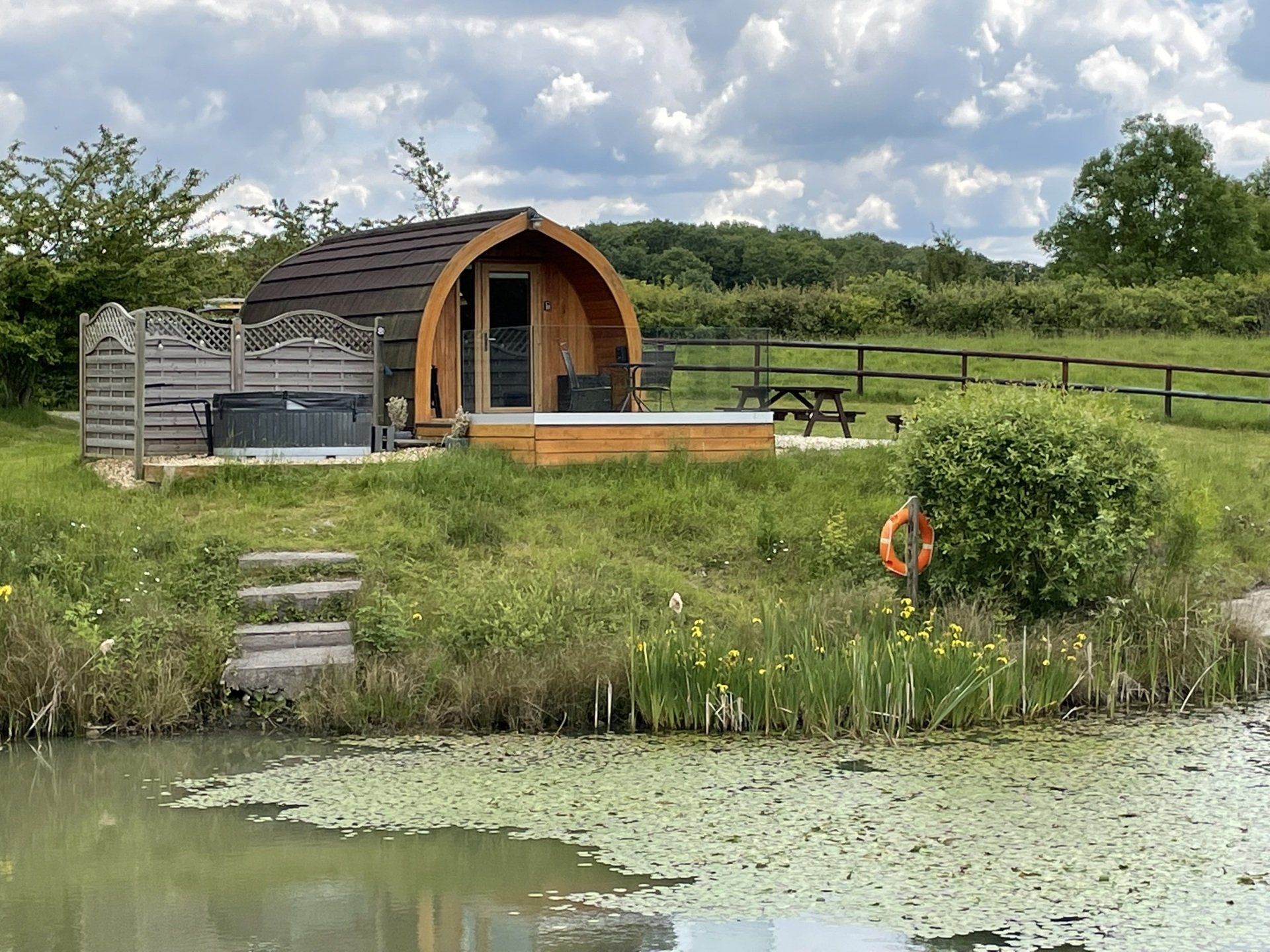 A wooden pod with a hot tub is sitting next to a pond.