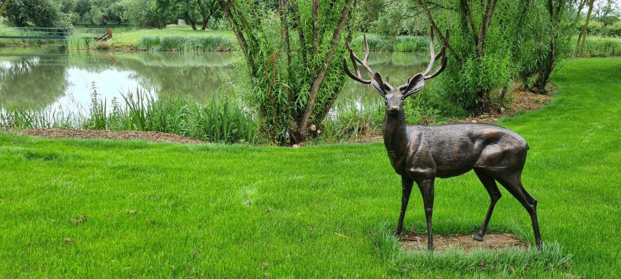 A bronze statue of a deer standing in a grassy field.