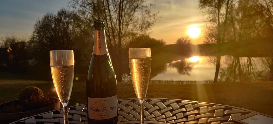 Two glasses of champagne and a bottle of champagne on a table with a sunset in the background.