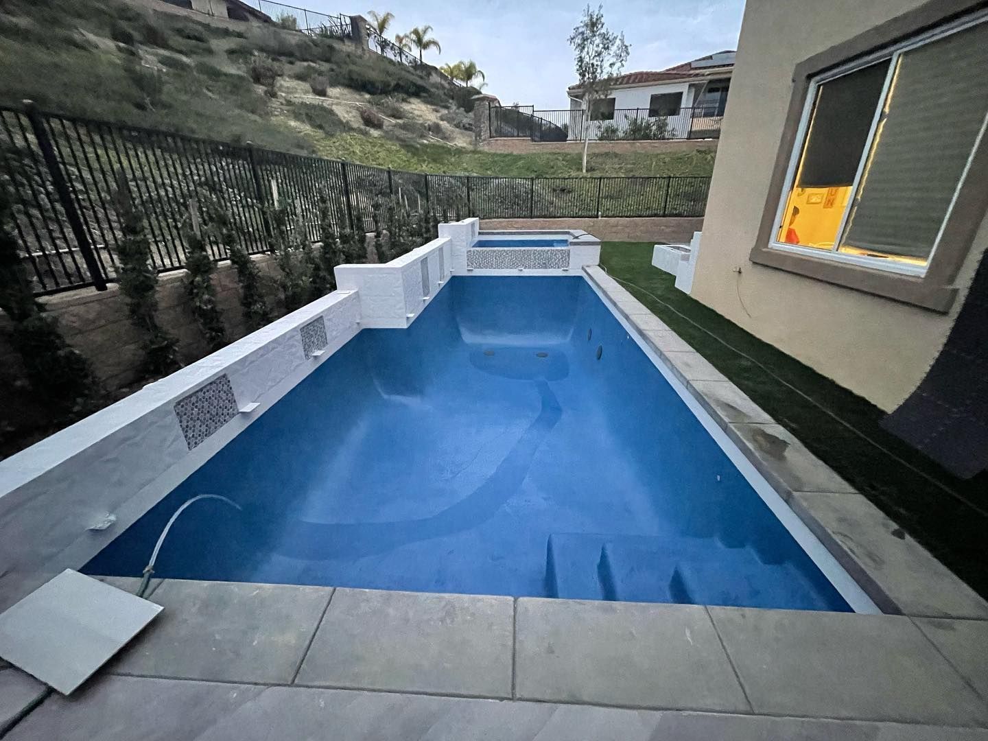 A large swimming pool is in the backyard of a house.