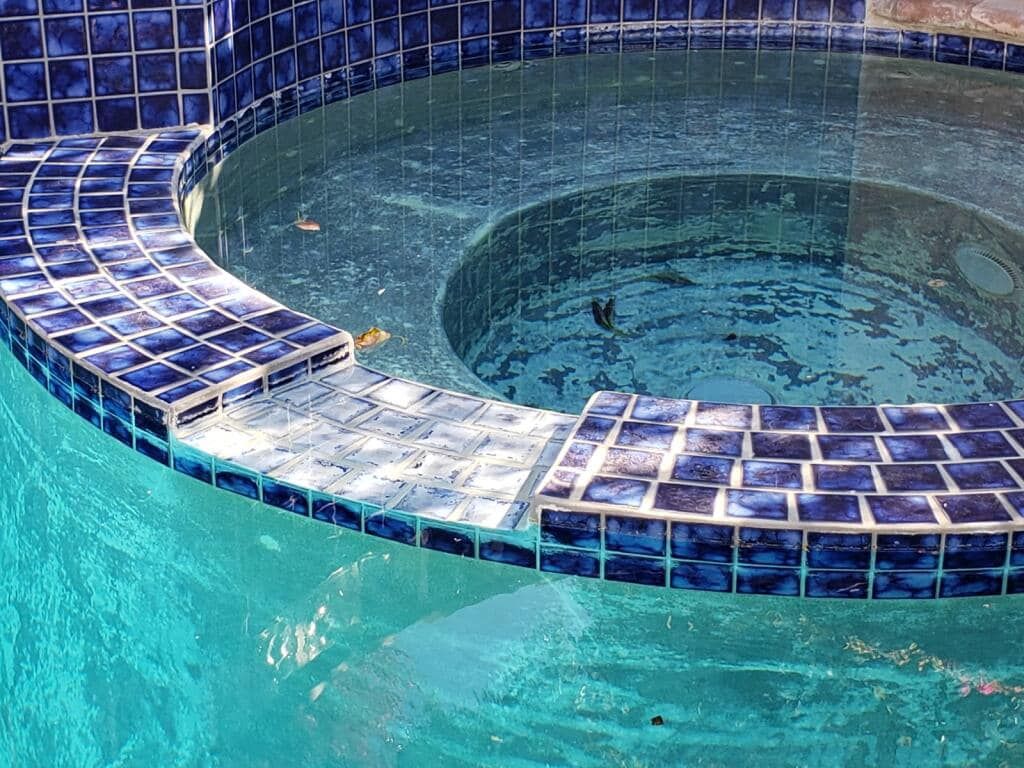 A swimming pool with a hot tub surrounded by blue tiles.
