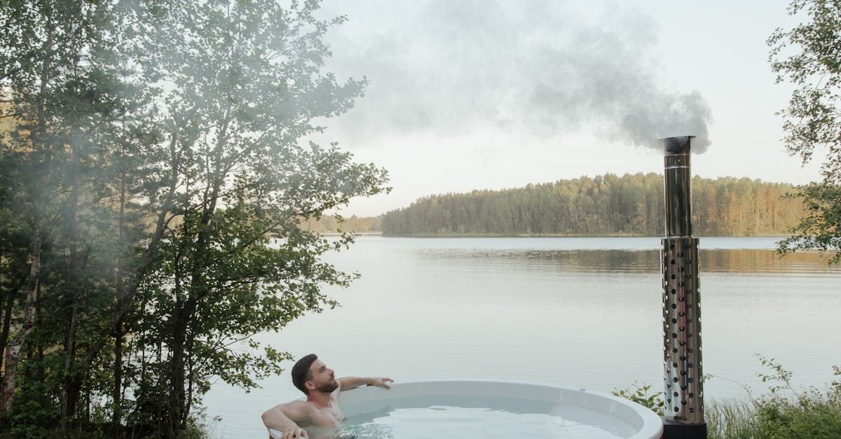 A man is taking a bath in a hot tub next to a lake.