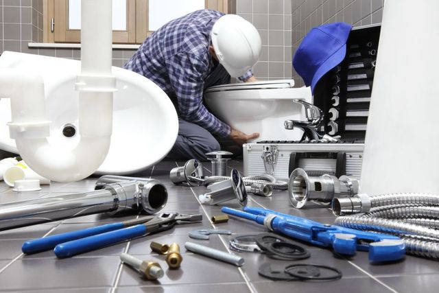 Plumber installing a toilet in a bathroom, surrounded by tools and plumbing parts.