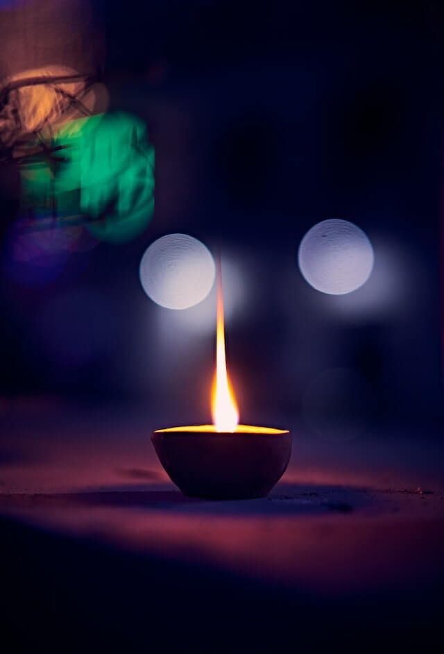 Lit oil lamp with a single flame glowing against a dark, blurred background with two soft lights.