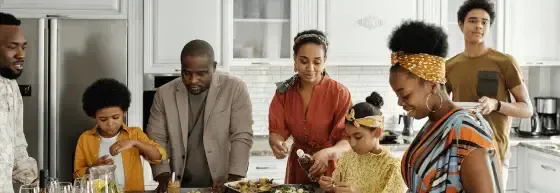 People gathered around a kitchen table preparing food, with bowls and ingredients spread out.