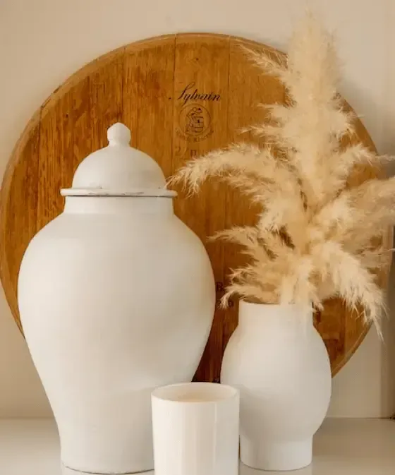 White ceramic vases and a candle on a shelf with a wooden tray and pampas grass.