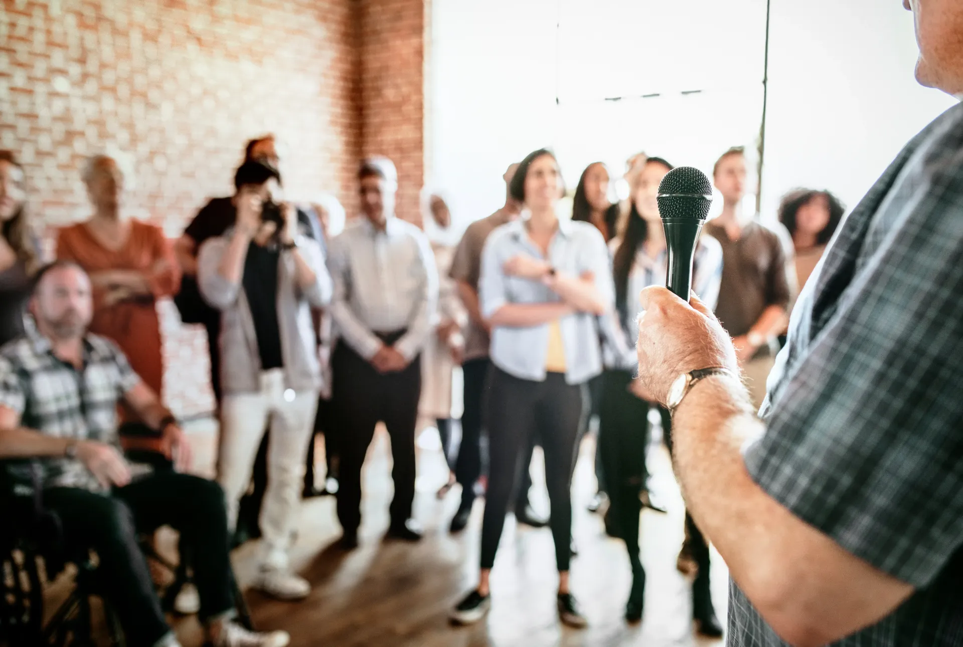 Person speaking to a group in a bright office, with several people standing and listening.