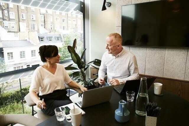 Two people talking at a table with a laptop in a bright office lounge