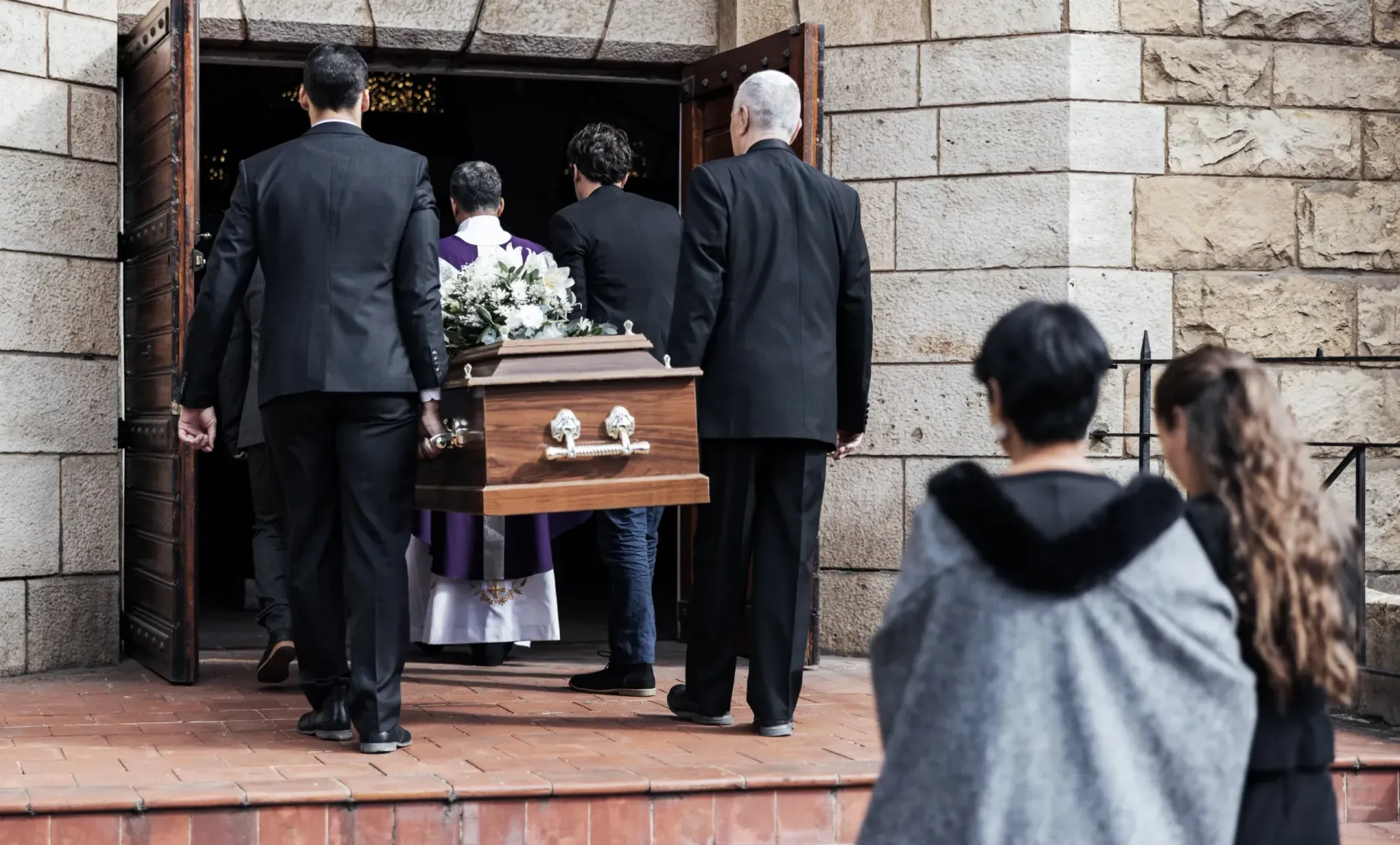 Mourners carry a coffin into a stone church during a funeral service