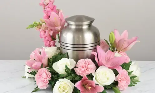 Silver urn surrounded by pink and white flowers on a light background