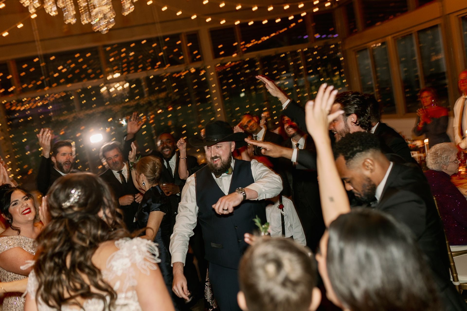 People dancing at a wedding reception, with string lights and a chandelier in the background.