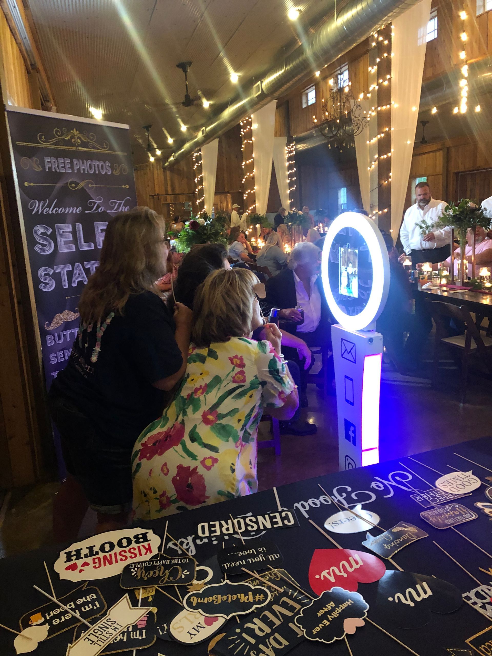 People taking photos at a photo booth with props, inside a decorated barn.
