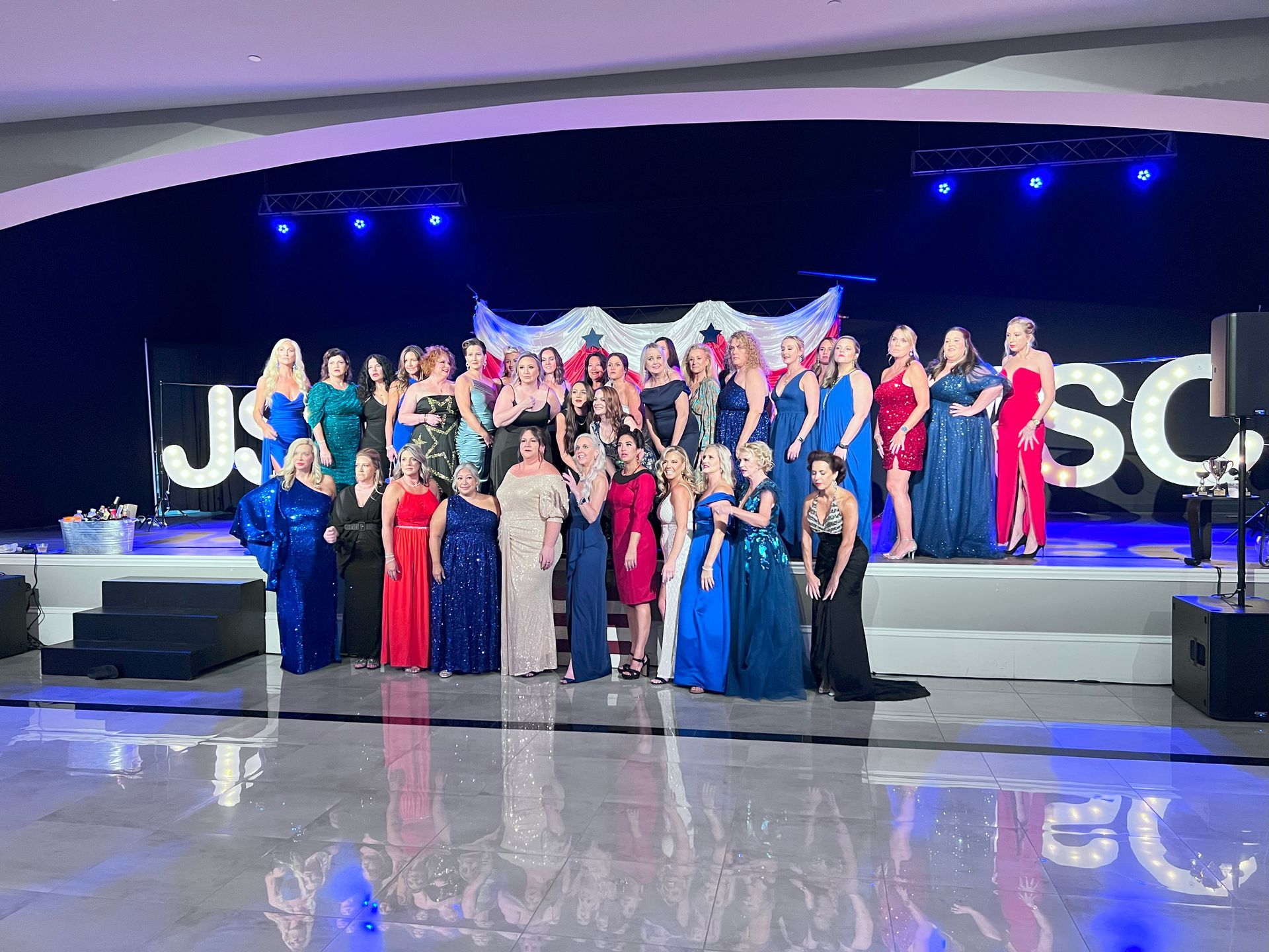 Group of people in formal attire on a stage with a stage backdrop and lighting.