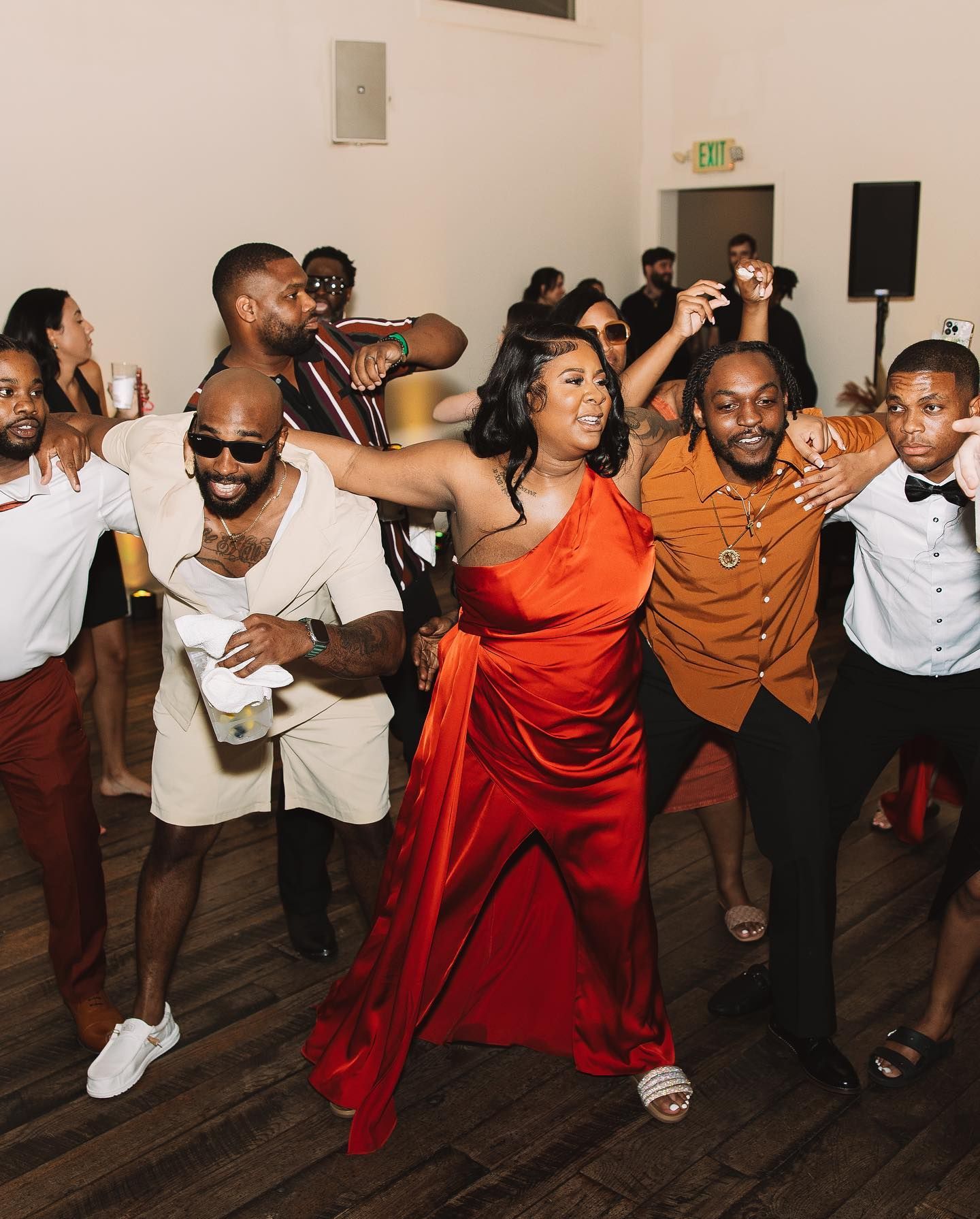 People dancing at an event. A woman in a red dress smiles, arms outstretched. Others surround her, smiling and dancing.