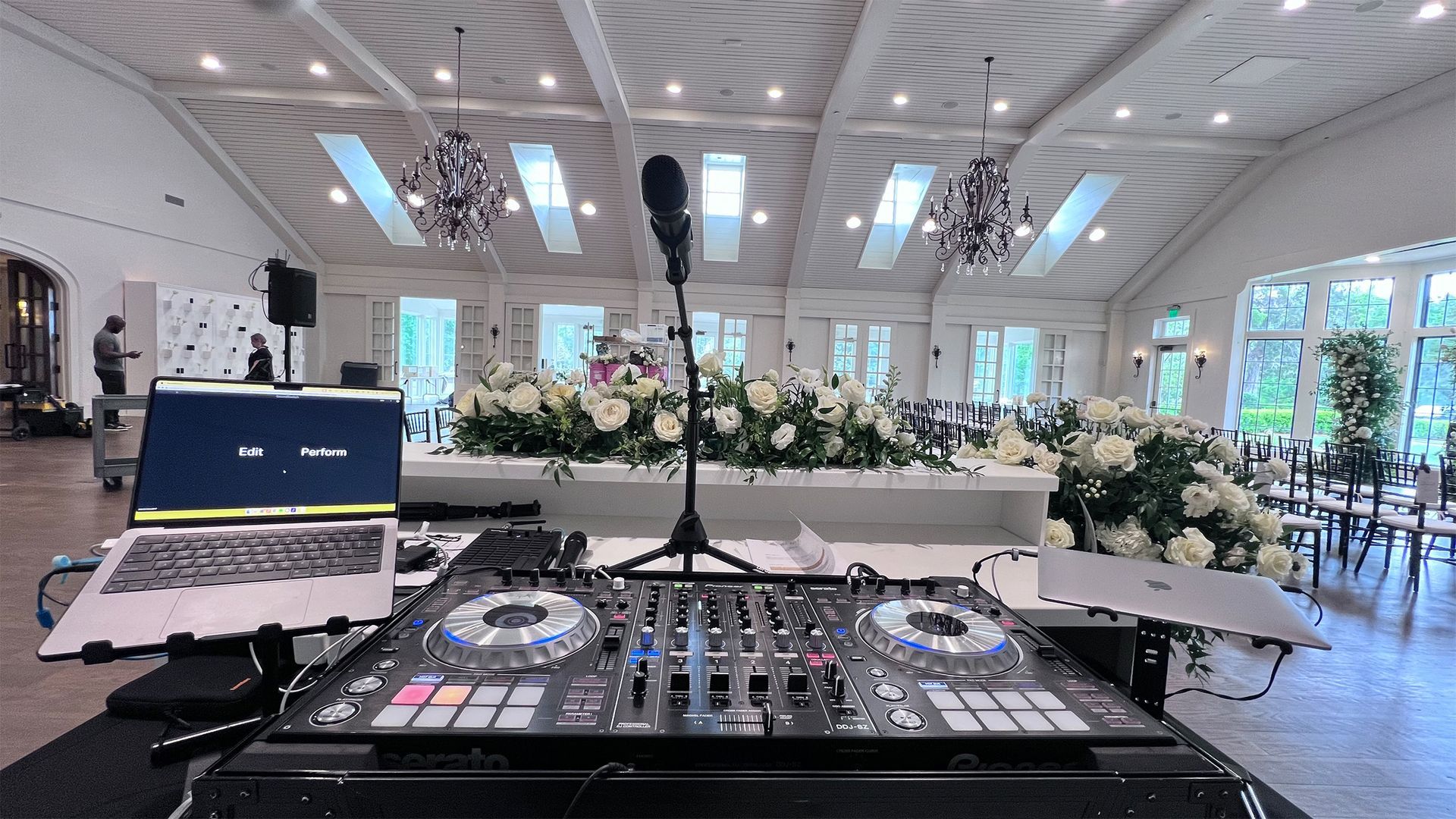 DJ setup with a microphone in a white ballroom decorated with flowers.