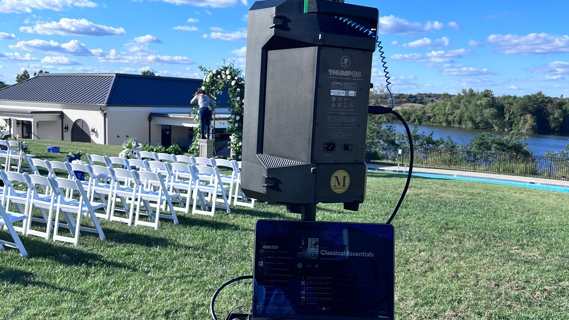Outdoor sound system setup at an event, with laptop and rows of chairs, overlooking a body of water.