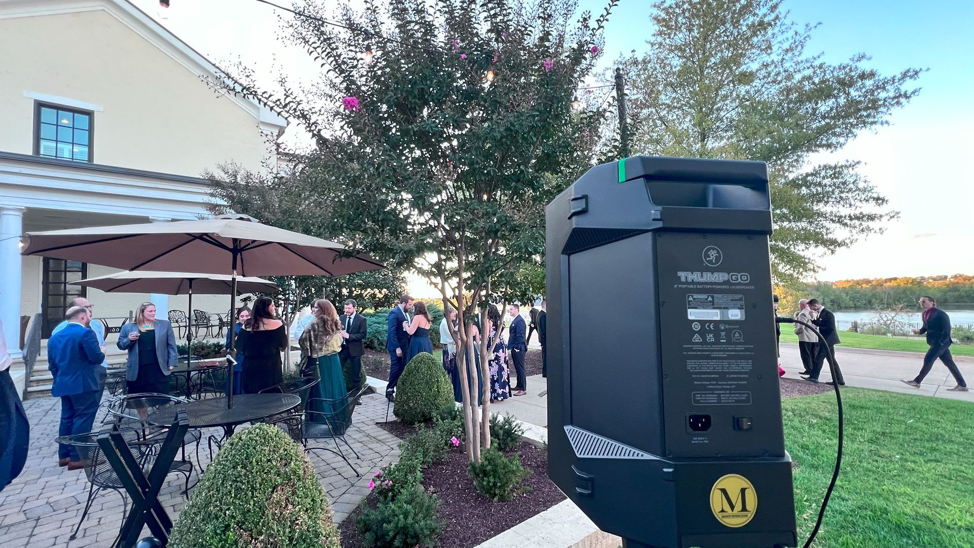 Black photo booth at outdoor event with people near a building and water.