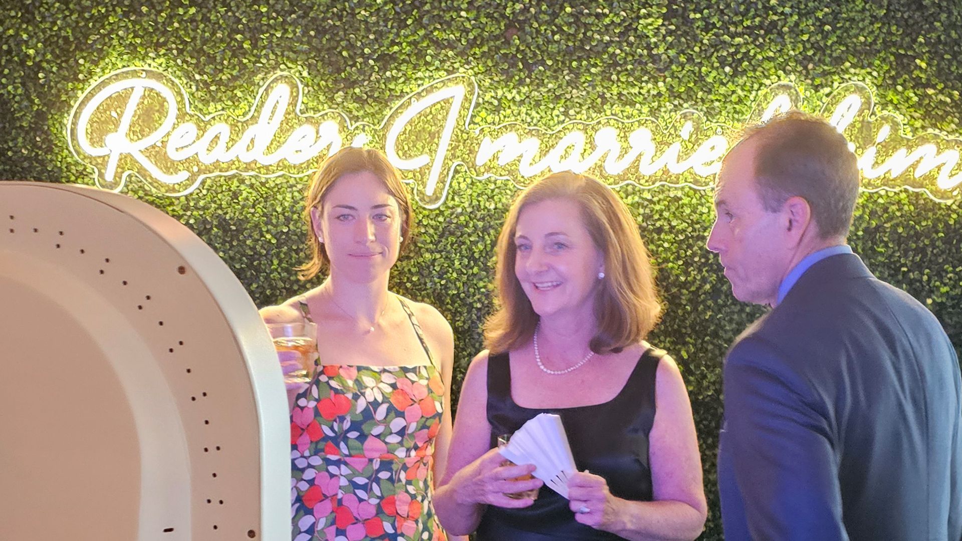 Three people pose in front of a neon sign that reads 