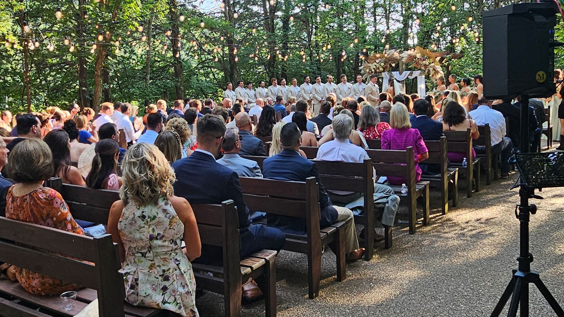 Wedding ceremony in a wooded area with guests seated on benches facing the altar.