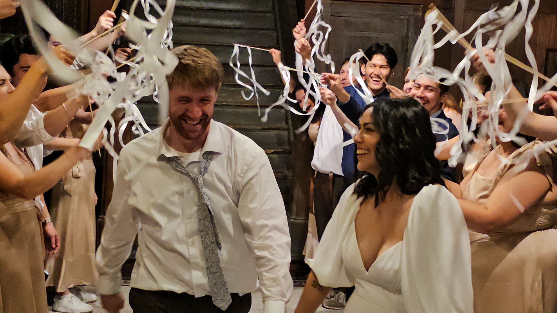 Newlyweds walk through guests holding up white streamers.