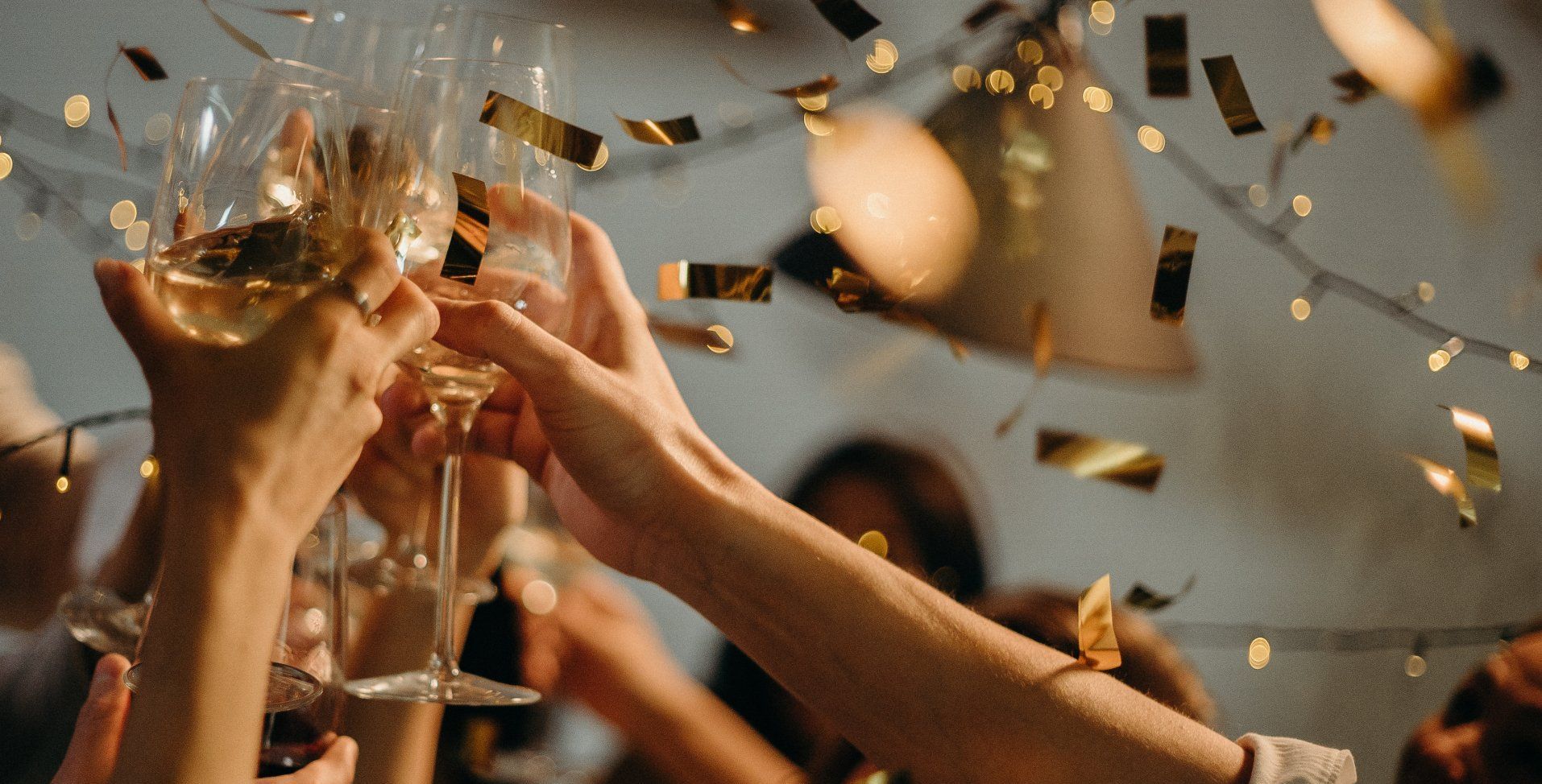 Hands toasting with champagne glasses, gold confetti falling.