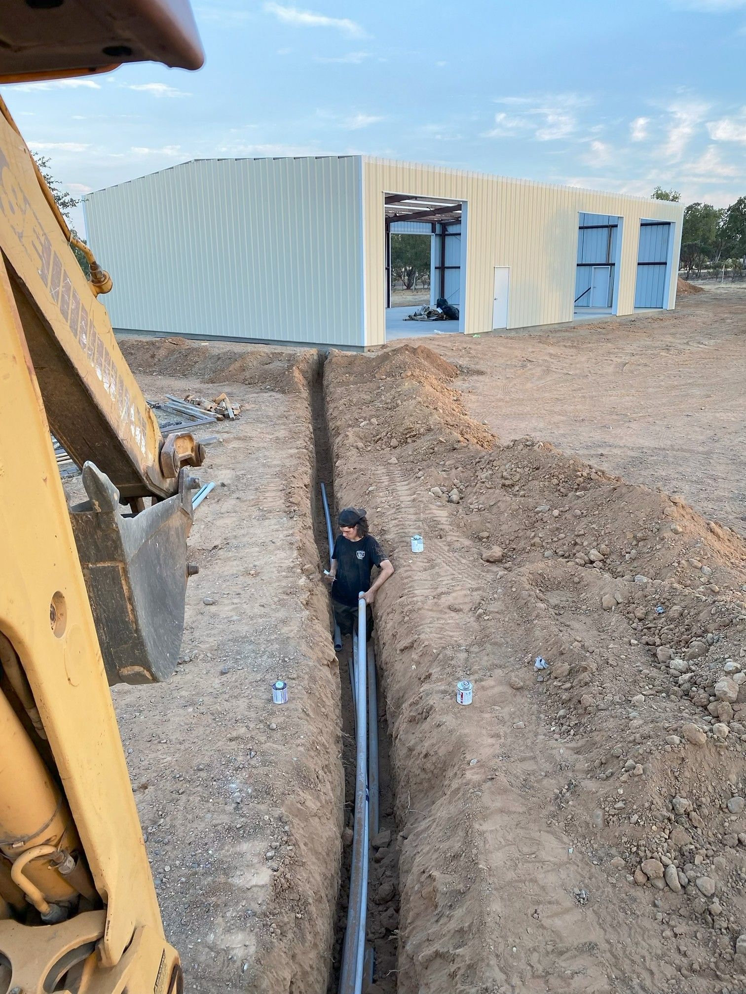 Construction site with a worker in a trench beside a corrugated metal building