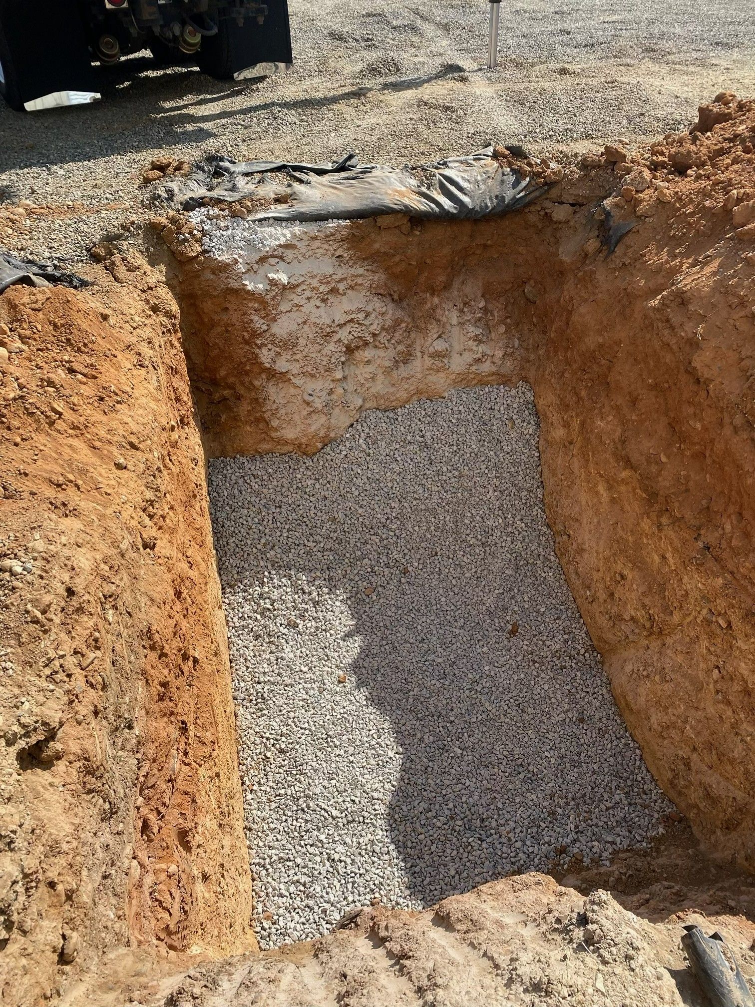 A freshly dug rectangular trench filled with gravel beside a paved surface.