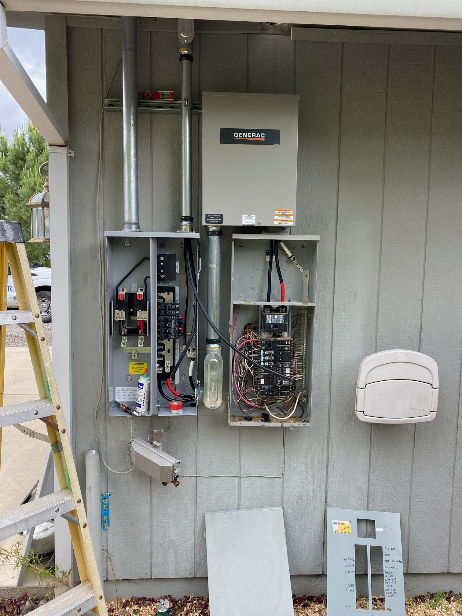 Open electrical service panels and utility meter boxes mounted on a gray exterior wall.