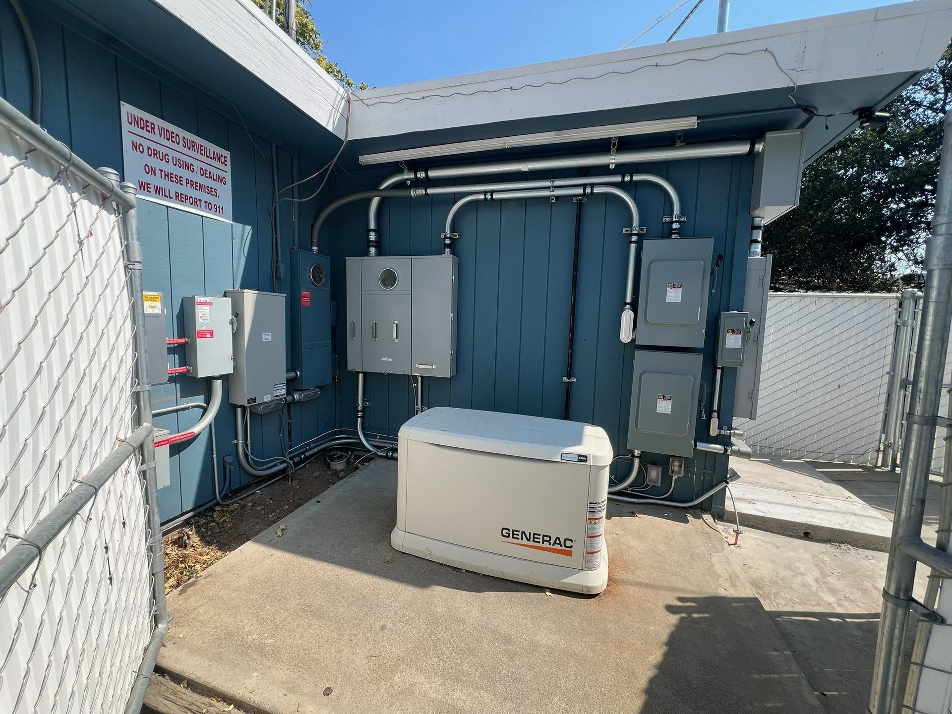 Blue utility building with electrical panels, conduit, and a large generator unit in front.