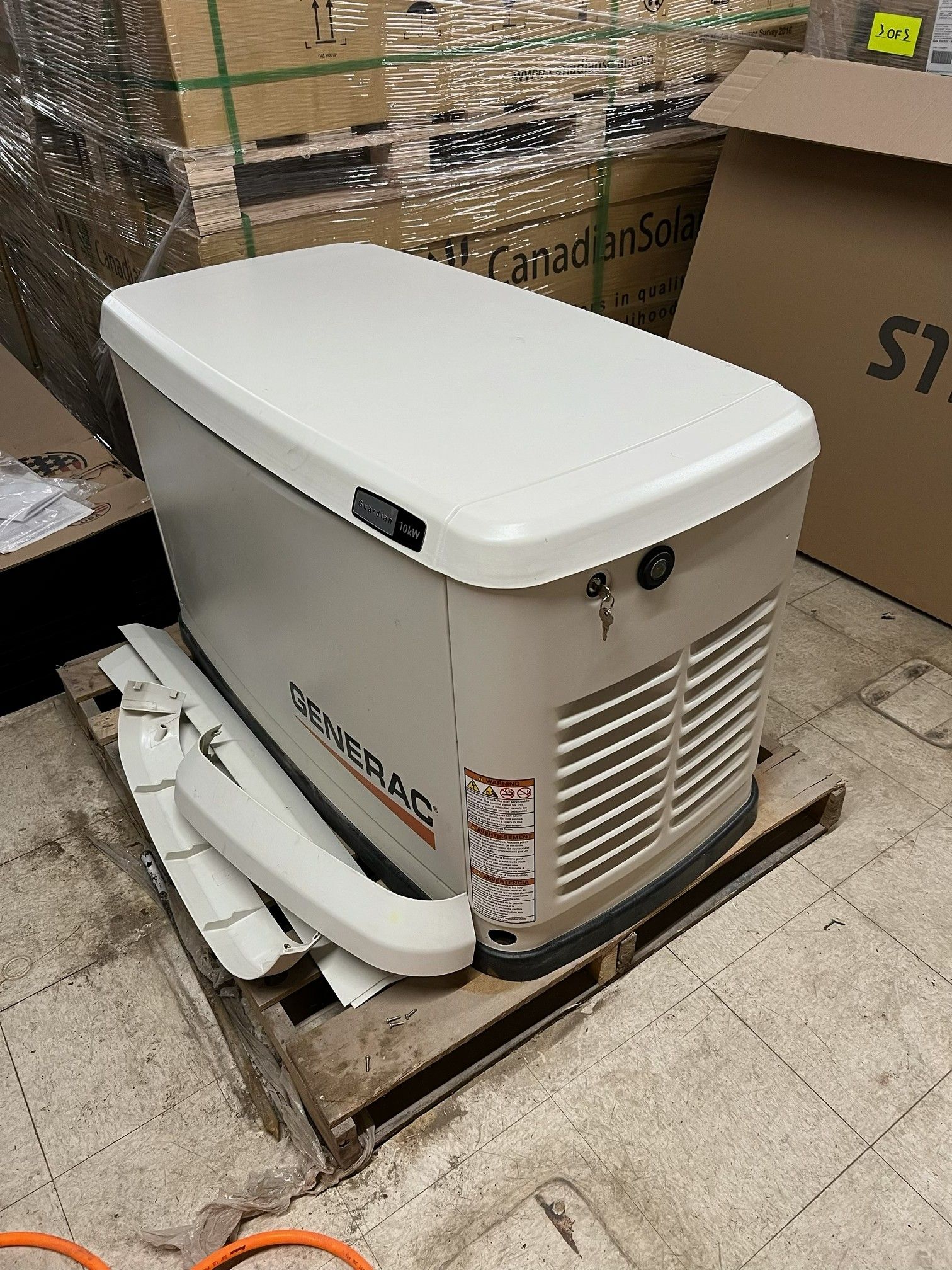 White portable generator or power unit on a pallet in a warehouse, with boxes in the background