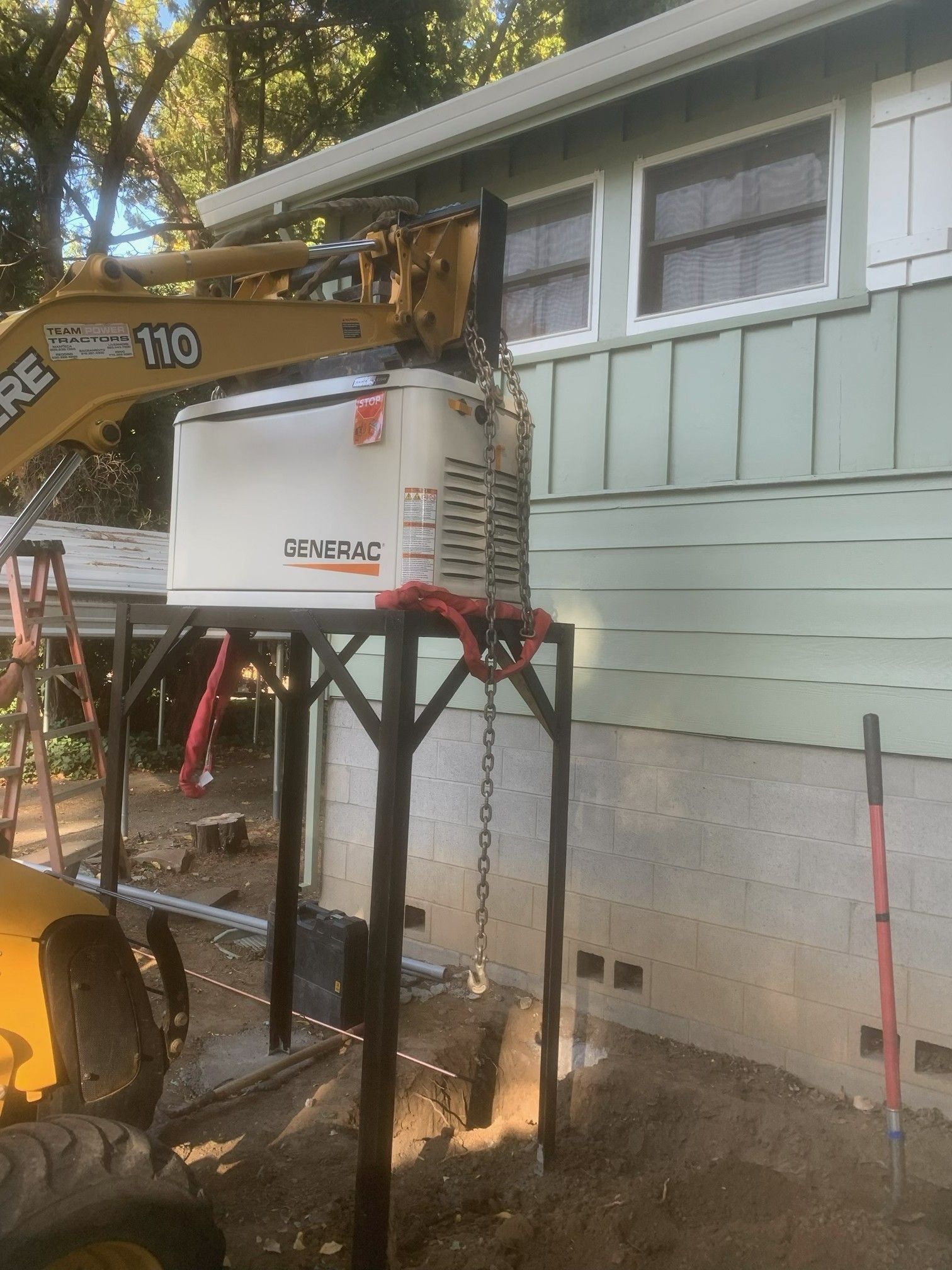 Yellow excavation machine drilling beside a raised house on stilts, with a white utility box nearby.