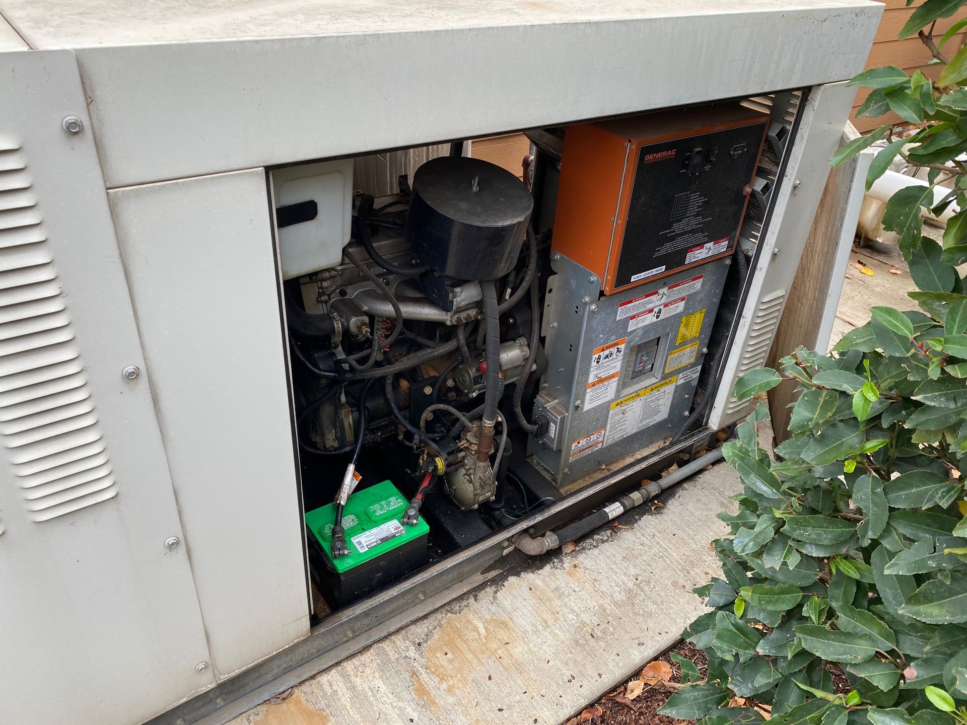 Open utility cabinet with exposed electrical and mechanical equipment beside a house.