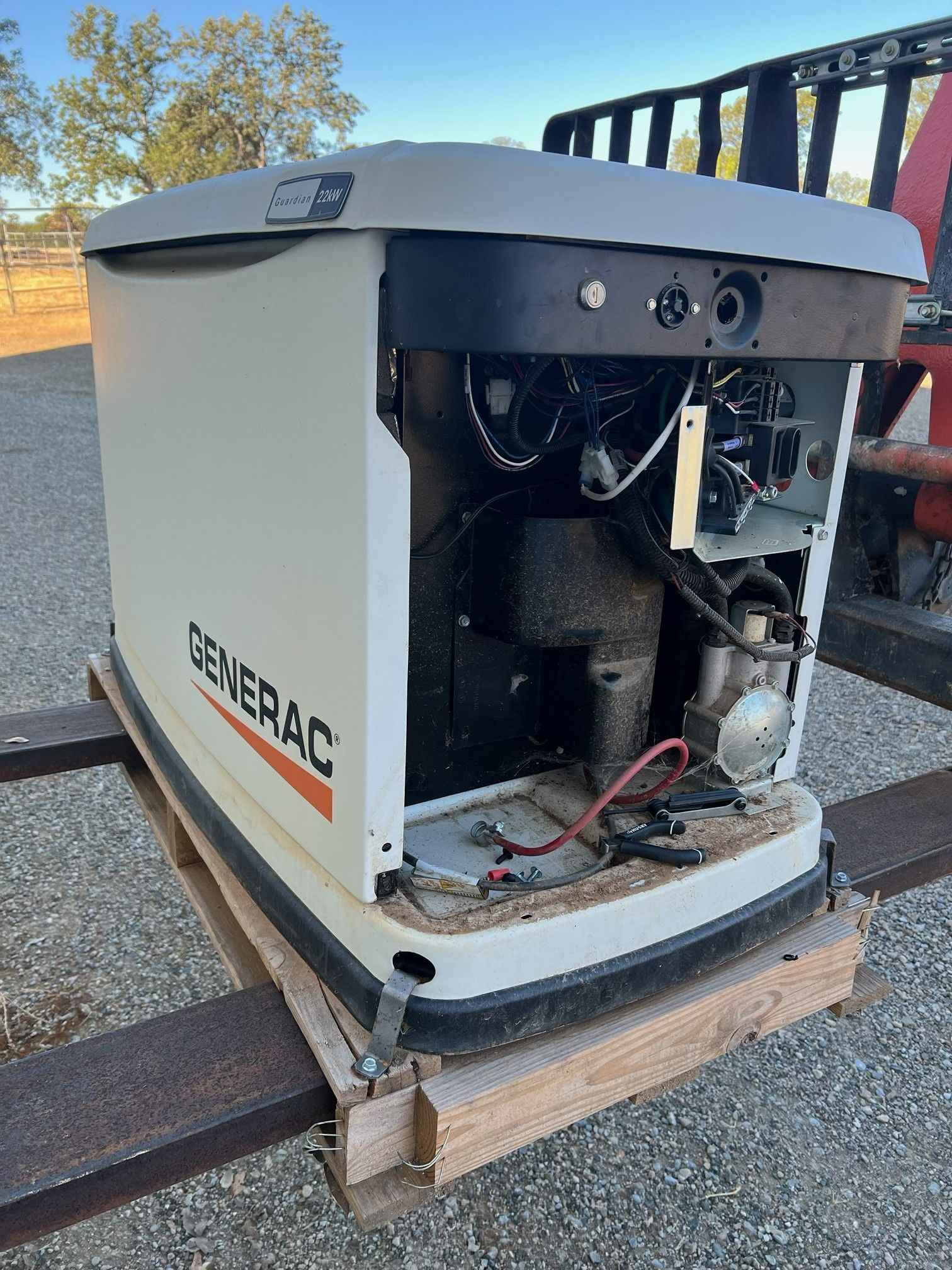 Damaged Generac generator with side panel open, exposing internal parts, outdoors on a pallet.