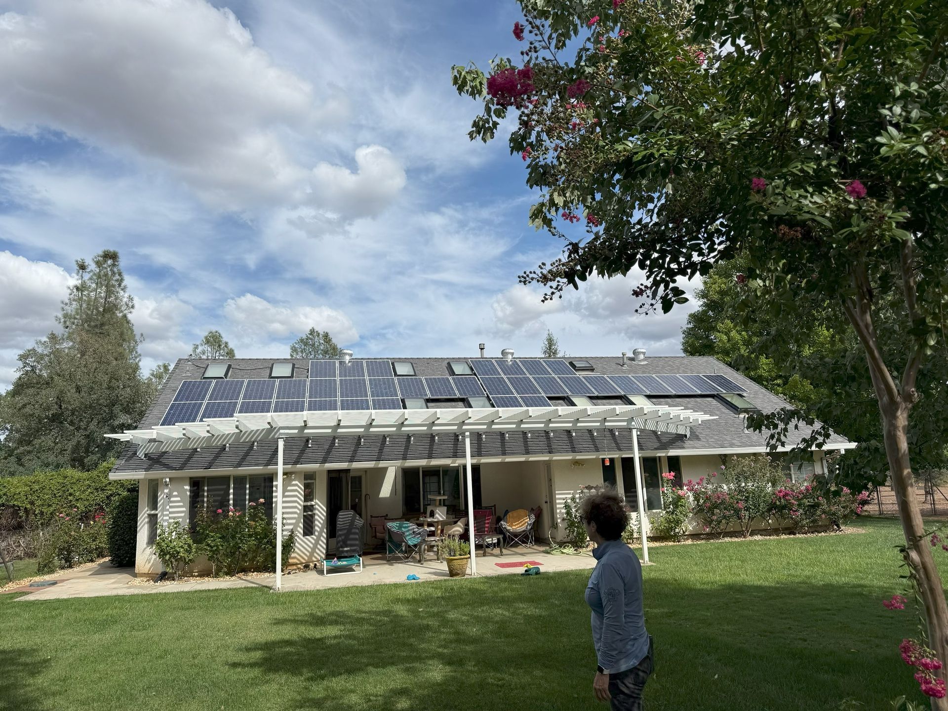 Person standing in a yard facing a solar-paneled house under a cloudy sky
