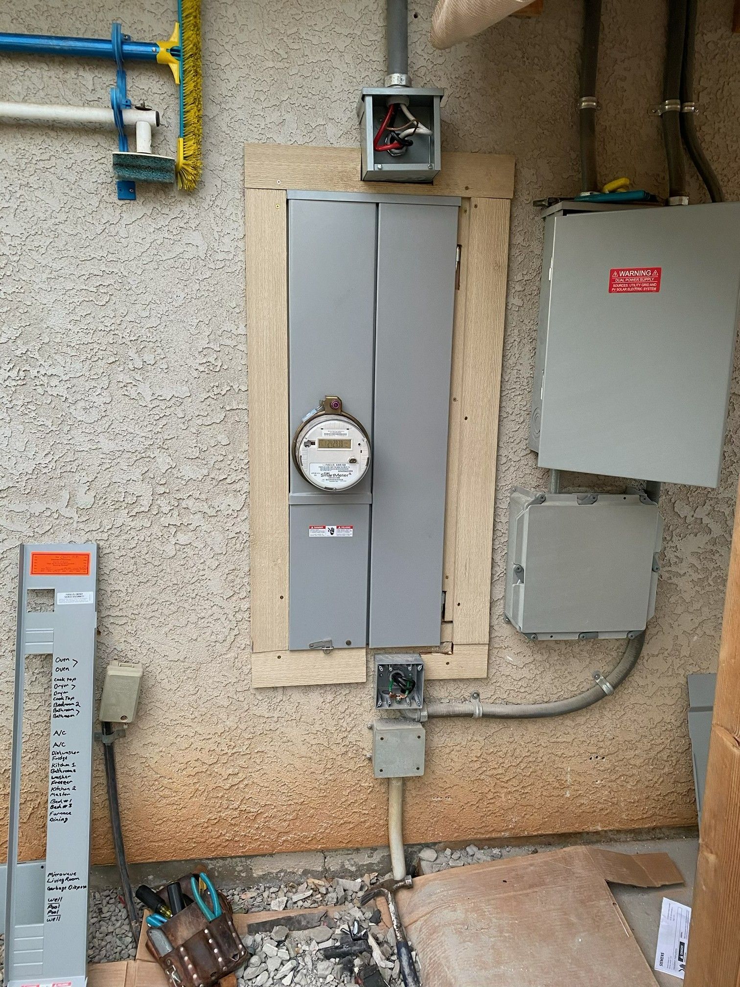 Outdoor utility meters and electrical panels mounted on a stucco wall, with a small electrical box above.