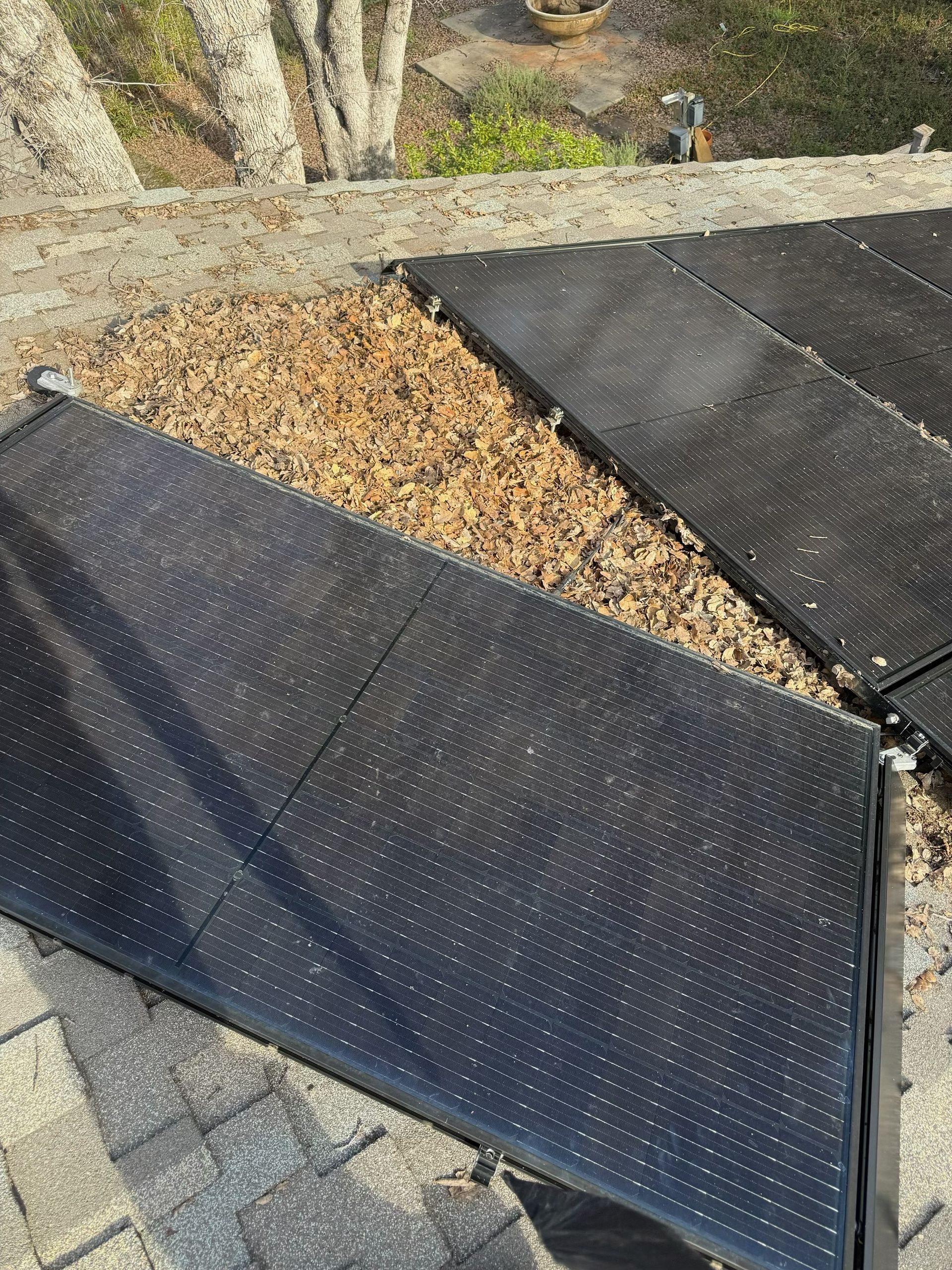 Black solar panel mats laid on a rooftop beside a gravel strip and stone wall.