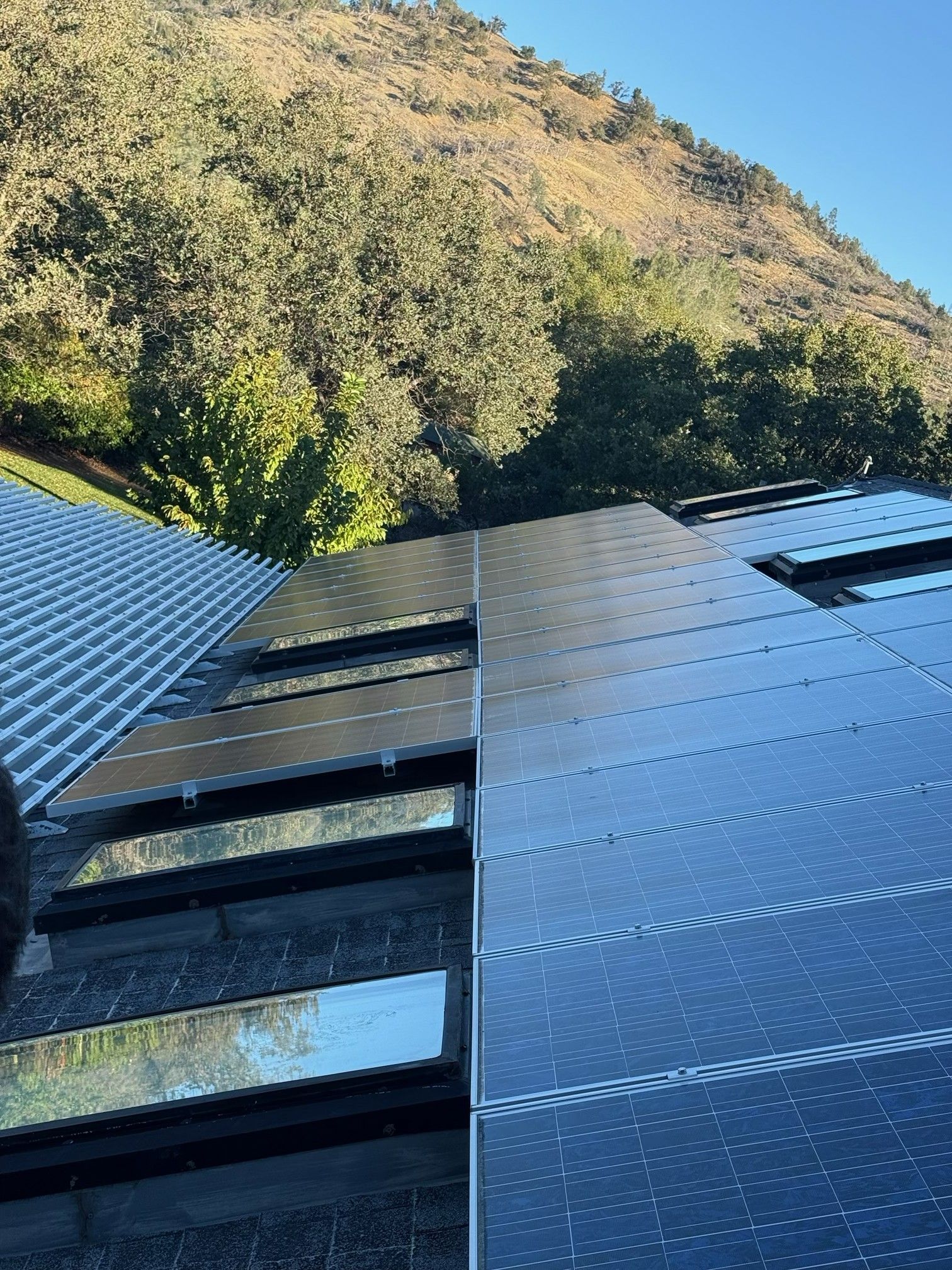 Modern black building facade beside a steep, tree-covered hillside under a clear blue sky
