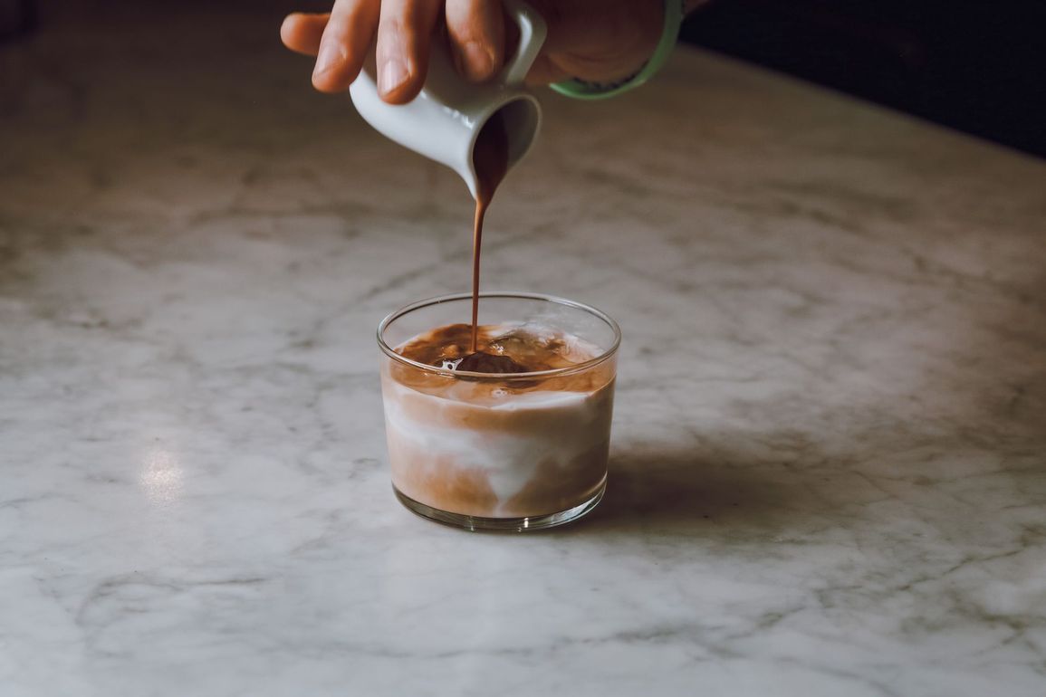 Versare a mano il caffè in un bicchiere con ghiaccio su un ripiano di marmo.