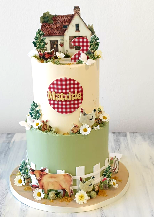Torta a due piani con crema, decorata con una casetta a scacchi rossi in cima e mucche, margherite e una staccionata alla base.