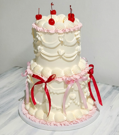 Elegante torta nuziale a più piani bianca con decorazioni rosa, ciliegie rosse e fiocchi di nastro rosso su un supporto rotondo.