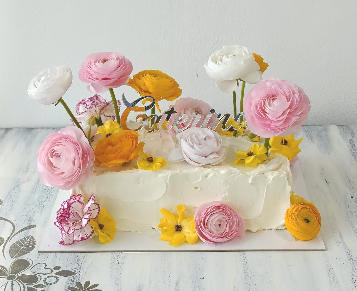Torta con glassa bianca decorata con fiori rosa, bianchi e gialli su un tavolo